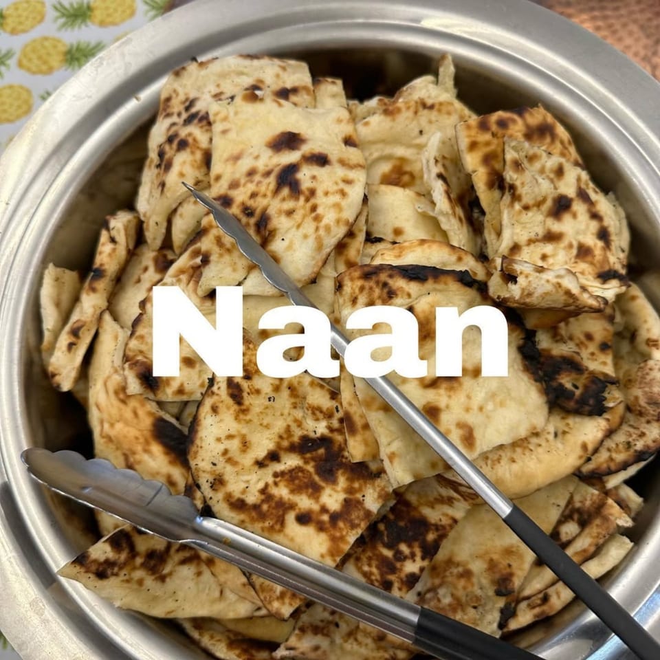 A metal serving dish filled with pieces of naan bread, with tongs resting inside.