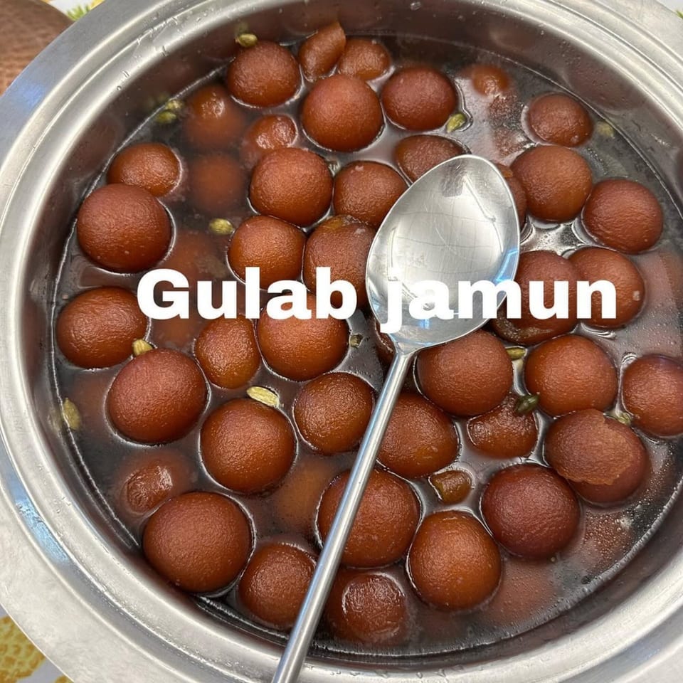 Gulab jamun, a traditional Indian dessert, in a metal bowl with a serving spoon.