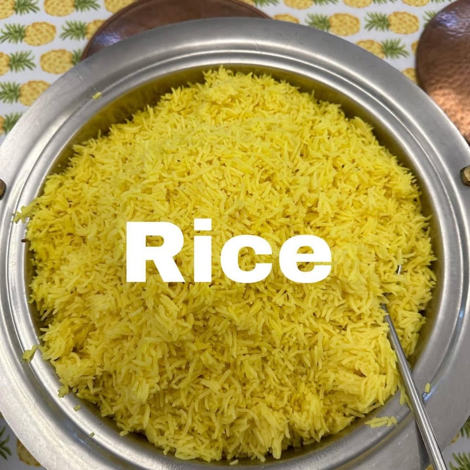 A large silver serving dish filled with bright yellow rice, with a serving spoon visible.